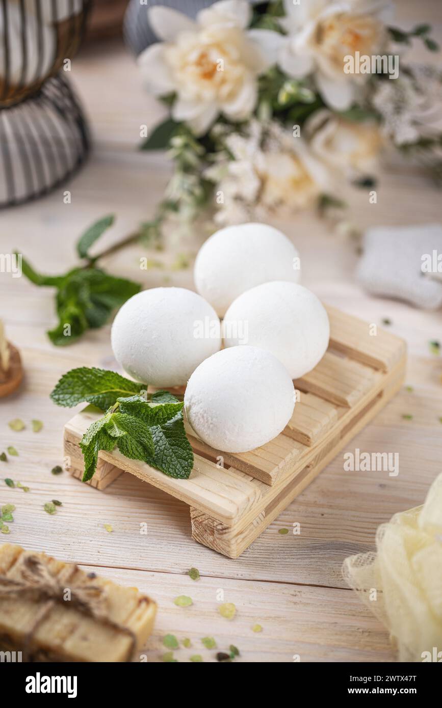 Élégantes bombes de bain disposées sur un plateau en bois orné de menthe fraîche et de doux fond floral Banque D'Images