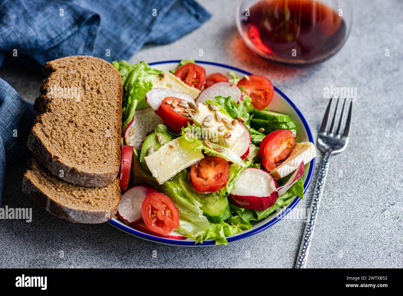 Gros plan de pain de seigle avec une salade de laitue, tomate, concombre, radis, brie et verre de vin rouge Banque D'Images