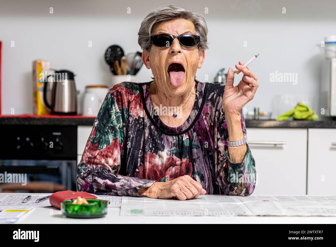 Femme assise à table avec une cigarette à la main en grimacant Banque D'Images