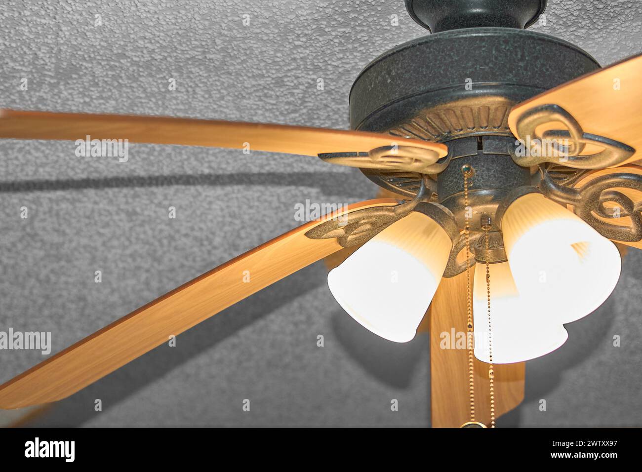 Gros plan d'un ventilateur de plafond doré avec des lumières allumées, ajoutant une touche d'élégance. Banque D'Images