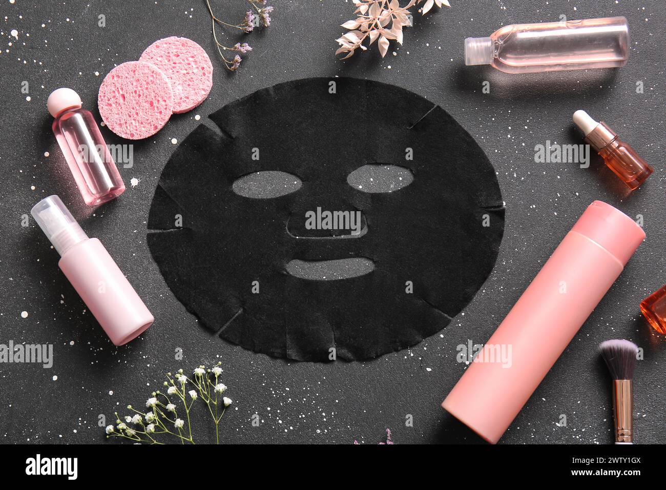 Masque de drap facial avec différents produits cosmétiques et fleurs de gypsophila sur fond noir Banque D'Images