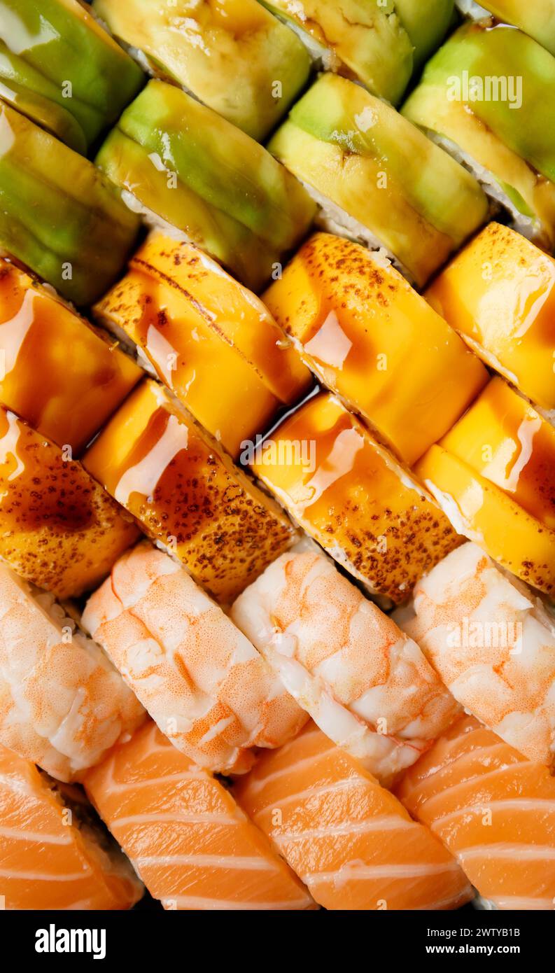 Ensemble de rouleaux de sushi multicolores brillants avec saumon, crevettes, avocat, fromage, vue de dessus, gros plan. Roule comme arrière-plan. Banque D'Images