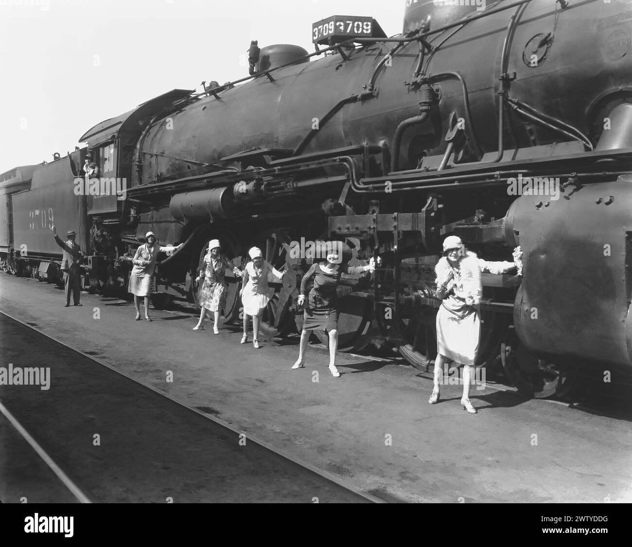 Photo publicitaire de cinq jeunes femmes avec le conducteur appuyé contre une locomotive de train rapide Banque D'Images