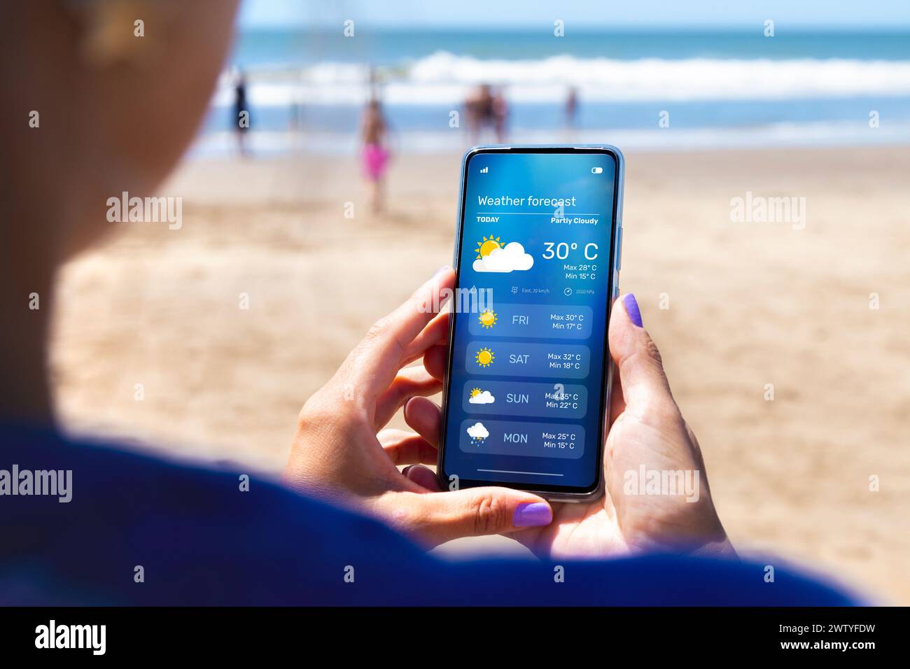 Femme à l'extérieur sur la plage en vérifiant les prévisions météorologiques sur une application sur son téléphone portable. Banque D'Images