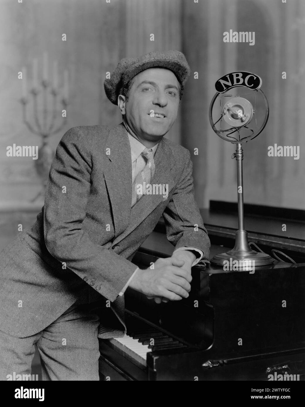 Musicien Ted Lewis dans un costume d'affaires et un chapeau appuyé sur un piano avec un microphone NBC à côté de lui Banque D'Images