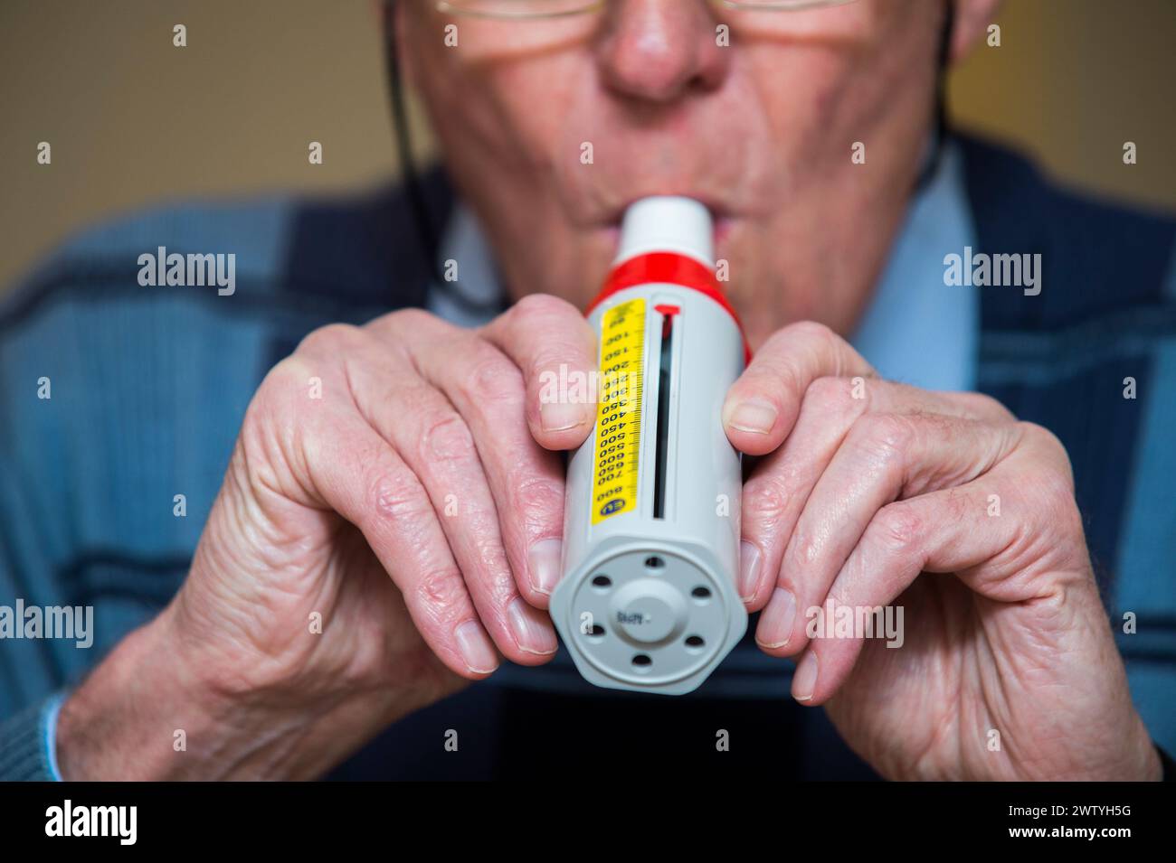 Un homme âgé souffle dans un débitmètre de pointe pour tester sa capacité pulmonaire. Banque D'Images