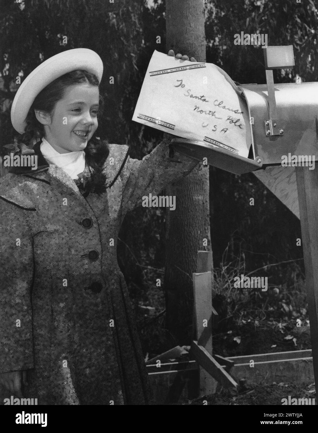 Fille dans un manteau d'hiver et chapeau à une boîte aux lettres postant une lettre au Père Noël Banque D'Images