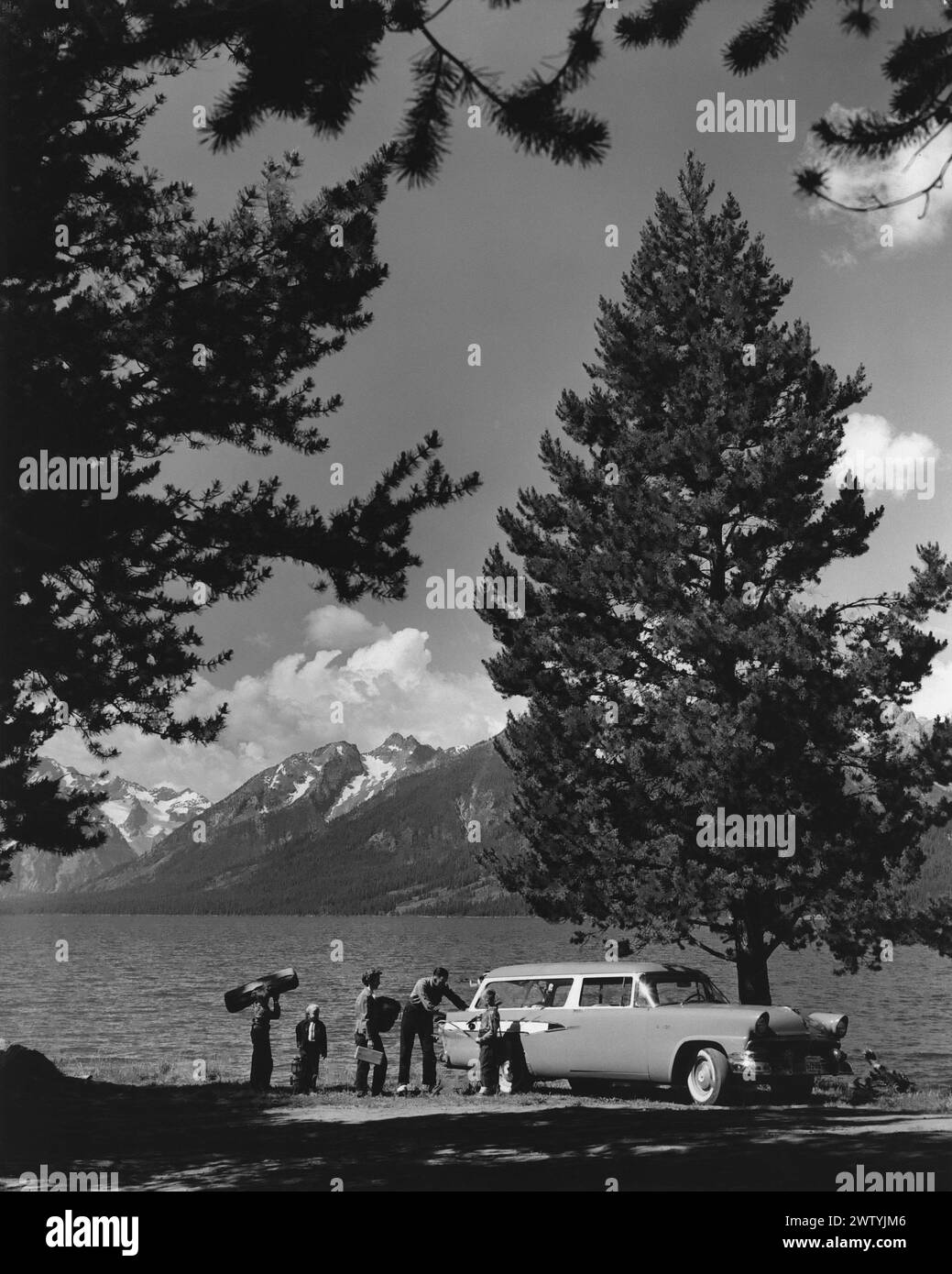 Jeune famille se préparant à installer le camp au bord du lac avec des montagnes enneigées en arrière-plan alors qu'ils sortent l'équipement de l'arrière de leur voiture familiale Banque D'Images