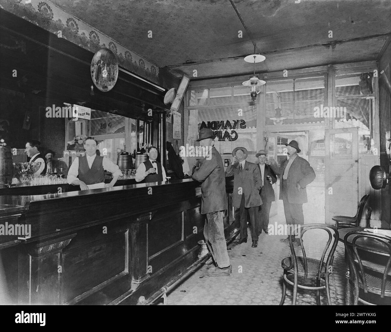 Des hommes en chapeaux debout au bar du Skandia Cafe dans le Minnesota au début du siècle tandis que des barmans se tiennent derrière le bar pour servir Banque D'Images