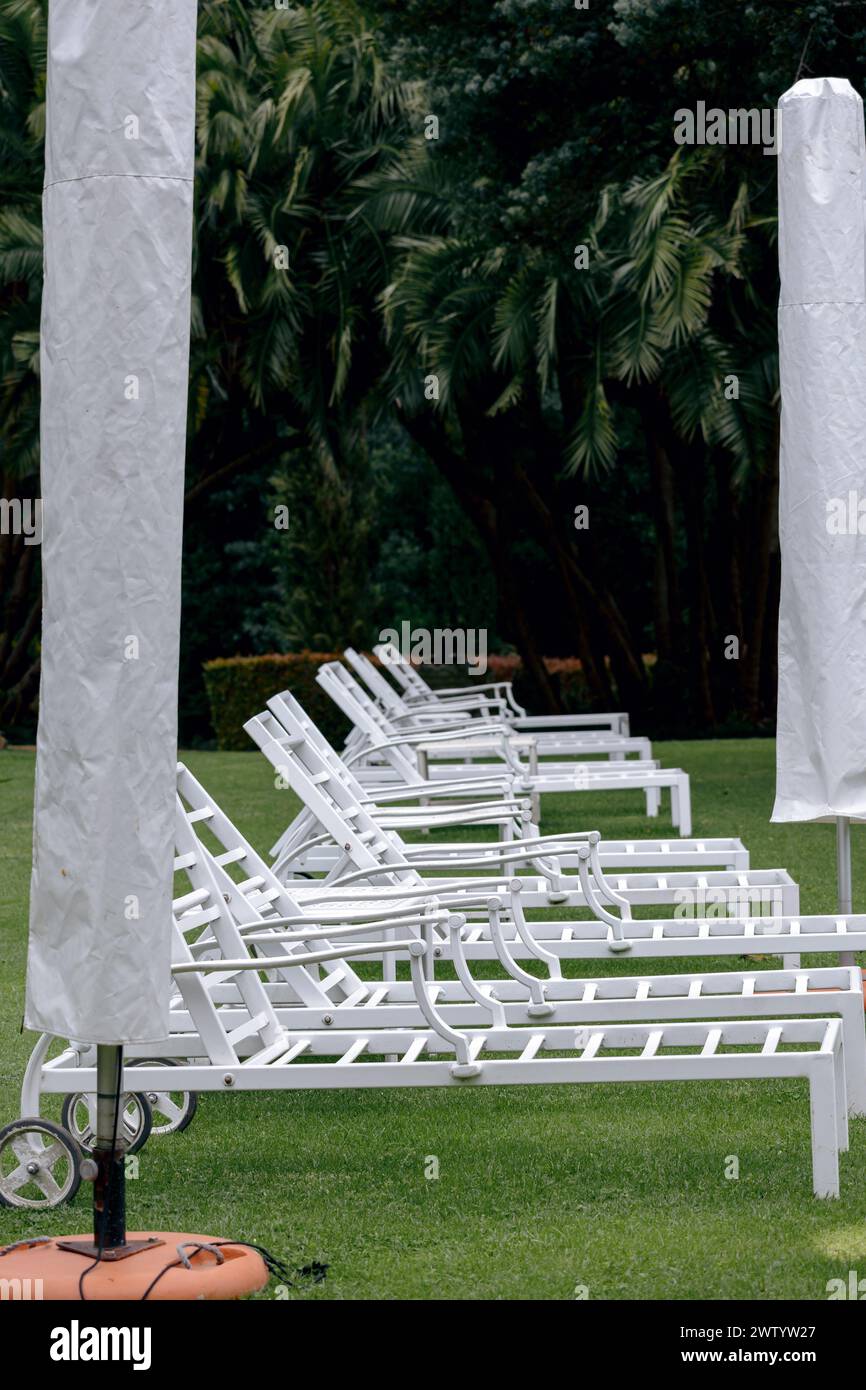 Préparation de la zone de l'hôtel pour la saison estivale, aménagement de mobilier de jardin pour la zone de la piscine de relaxation. Chaises longues en plastique blanc et parapluie Banque D'Images