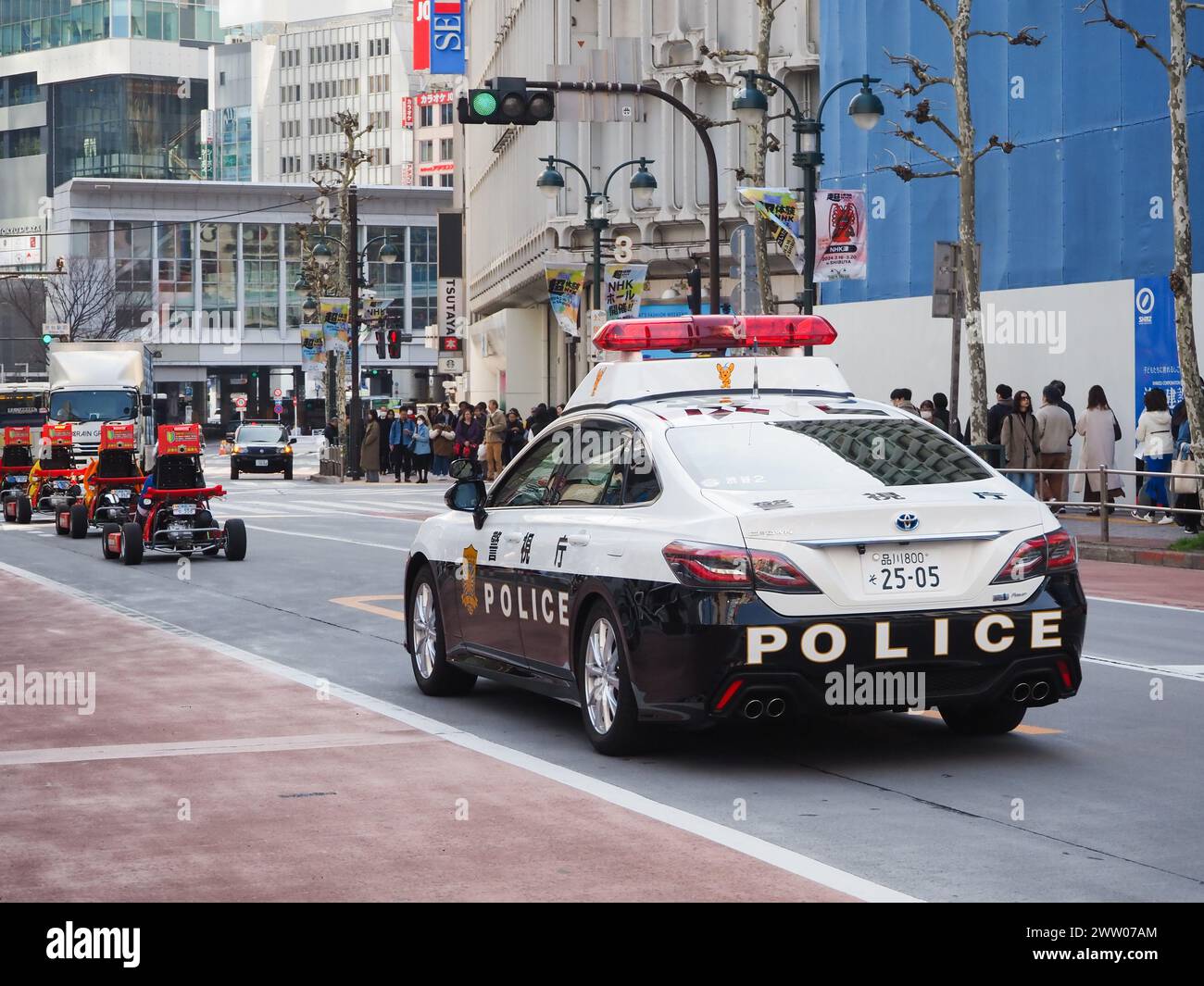 TOKYO, JAPON - 19 mars 2024 : une voiture de police conduisant derrière une file de karting de location sur une route près de la gare de Shibuya à Tokyo. Banque D'Images