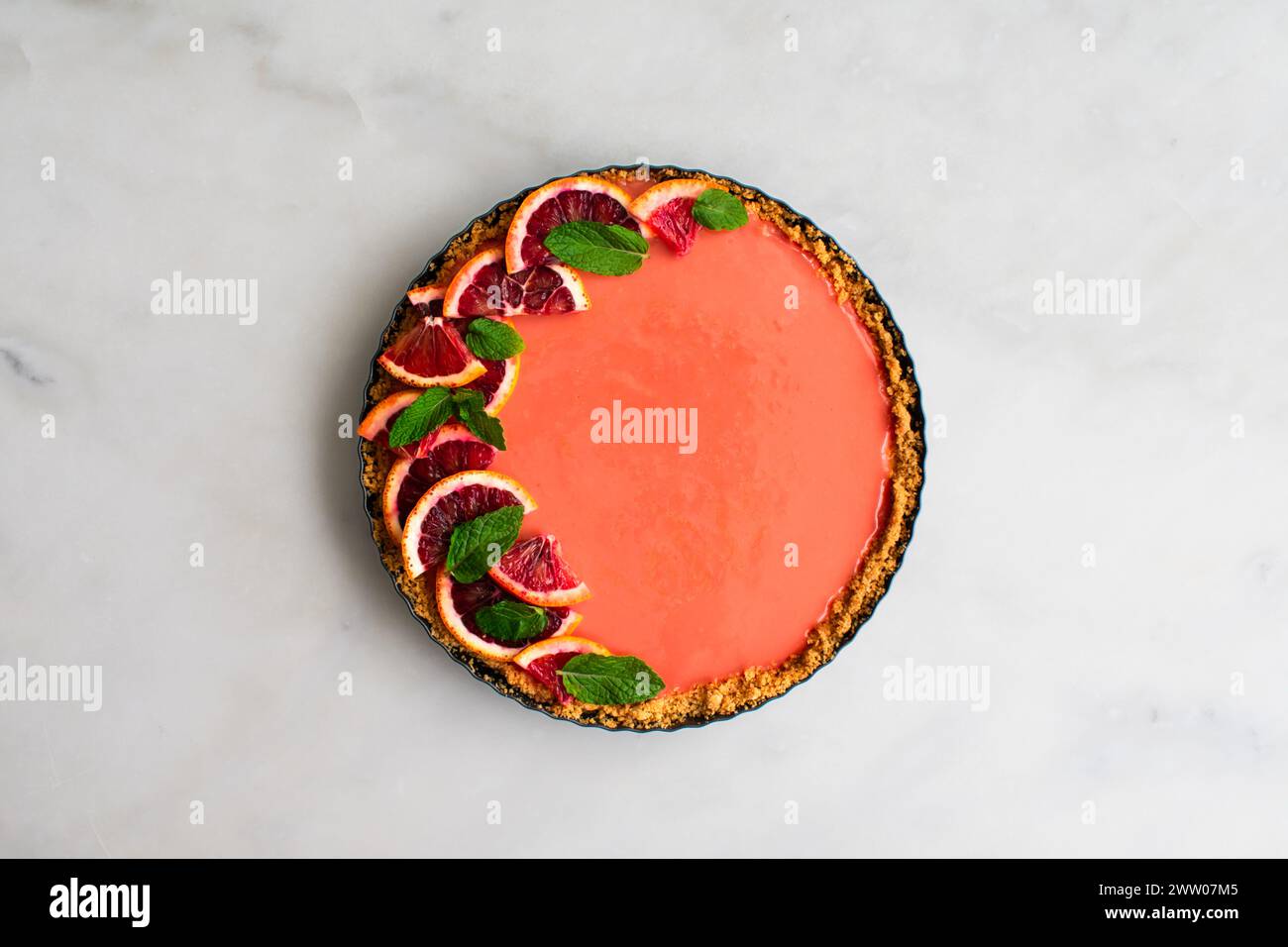 Tarte au cheesecake à l'orange sanguine sur une table en marbre blanc : tarte au cheesecake au caillé à l'orange framboise garnie de feuilles de menthe dans une croûte de craquelins graham Banque D'Images