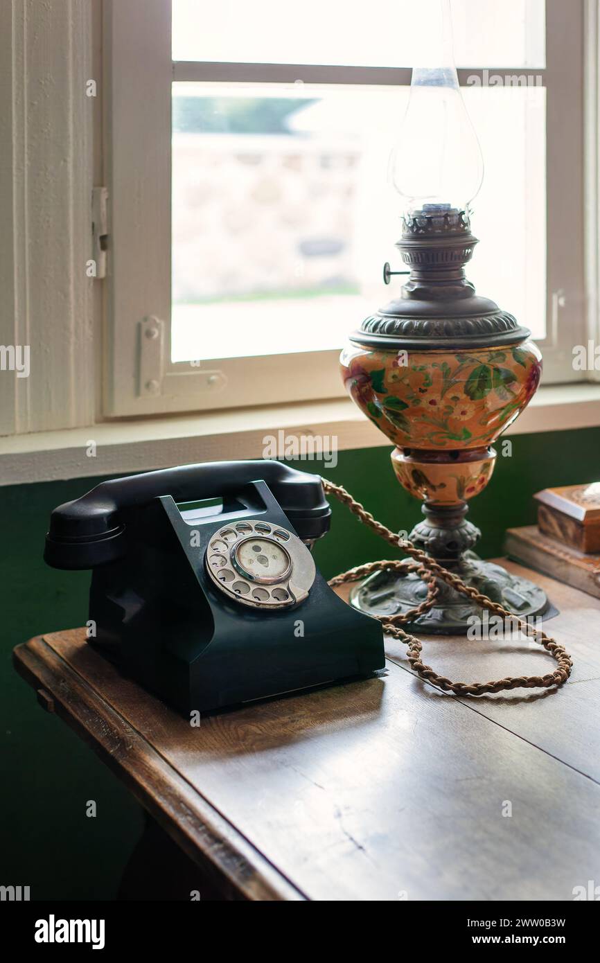 Téléphone noir vintage près de la fenêtre avec vieilli une grande lampe au kérosène sur le bureau en bois. Banque D'Images