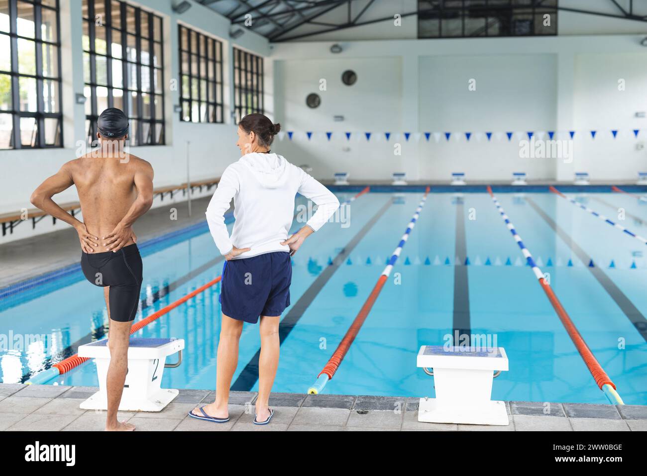 Un entraîneur diversifié et un athlète masculin nageur se tiennent près de la piscine, prêt à nager, avec un espace de copie Banque D'Images