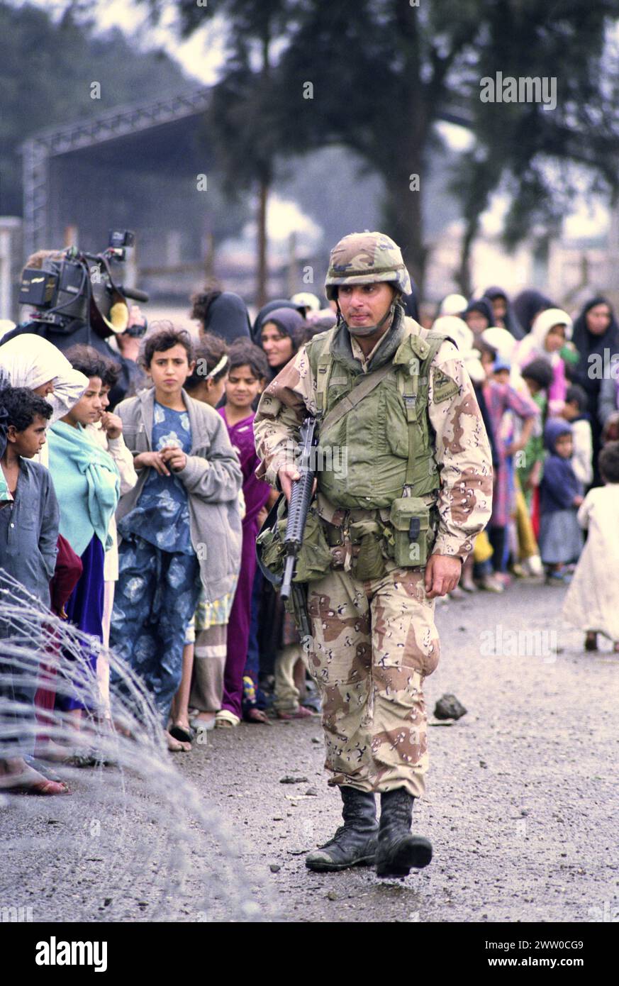 23 mars 1991 Un soldat de l'armée américaine de la 3ème division blindée 'fer de lance' garde une ligne ordonnée d'Irakiens déplacés, faisant la queue pour de la nourriture et des boissons près de Safwan dans le sud de l'Irak. Banque D'Images