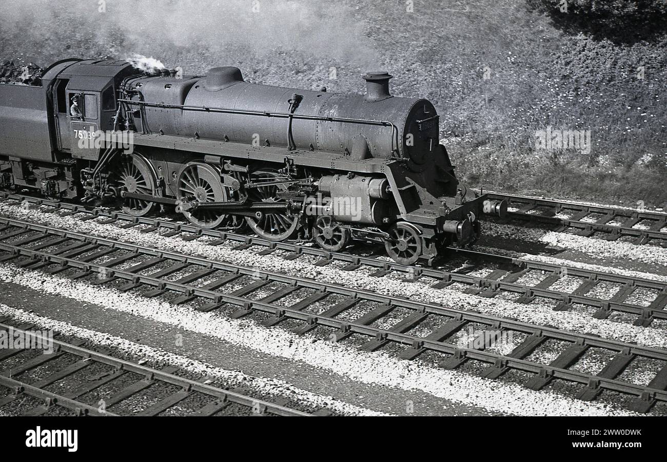 Années 1950, historique, Briitsh Railways locomotive à vapeur, 75039 sur la voie ferrée, Angleterre, Royaume-Uni, conducteur de train en cabine. Construite à Swindon Works et introduite pour la première fois en 1951 pour la nouvelle Briitsh Railways, la locomotive 75039 était une BR Standard Class 4, une version plus petite et plus légère de la Standard Class 5 7300. Construit en 1953, il a d'abord été affecté à la ligne Bletchley (1E), continuant en service jusqu'en 1967, avant d'être mis au rebut l'année suivante. Banque D'Images