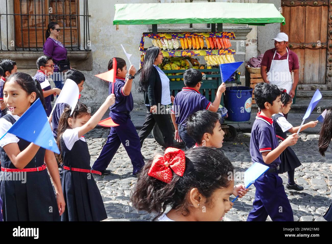 Antigua, Guatemala. 20 mars 2024. Les écoliers escortent la Semana Santa Festival Queen, devant un vendeur de fruits alors qu'ils défilent dans le centre historique en préparation de la semaine de la houle, le 20 mars 2024 à Antigua, au Guatemala. Les processions opulentes, les algèbres détaillées et les traditions séculaires attirent plus d'un million de personnes dans l'ancienne capitale. Crédit : Richard Ellis/Richard Ellis/Alamy Live News Banque D'Images