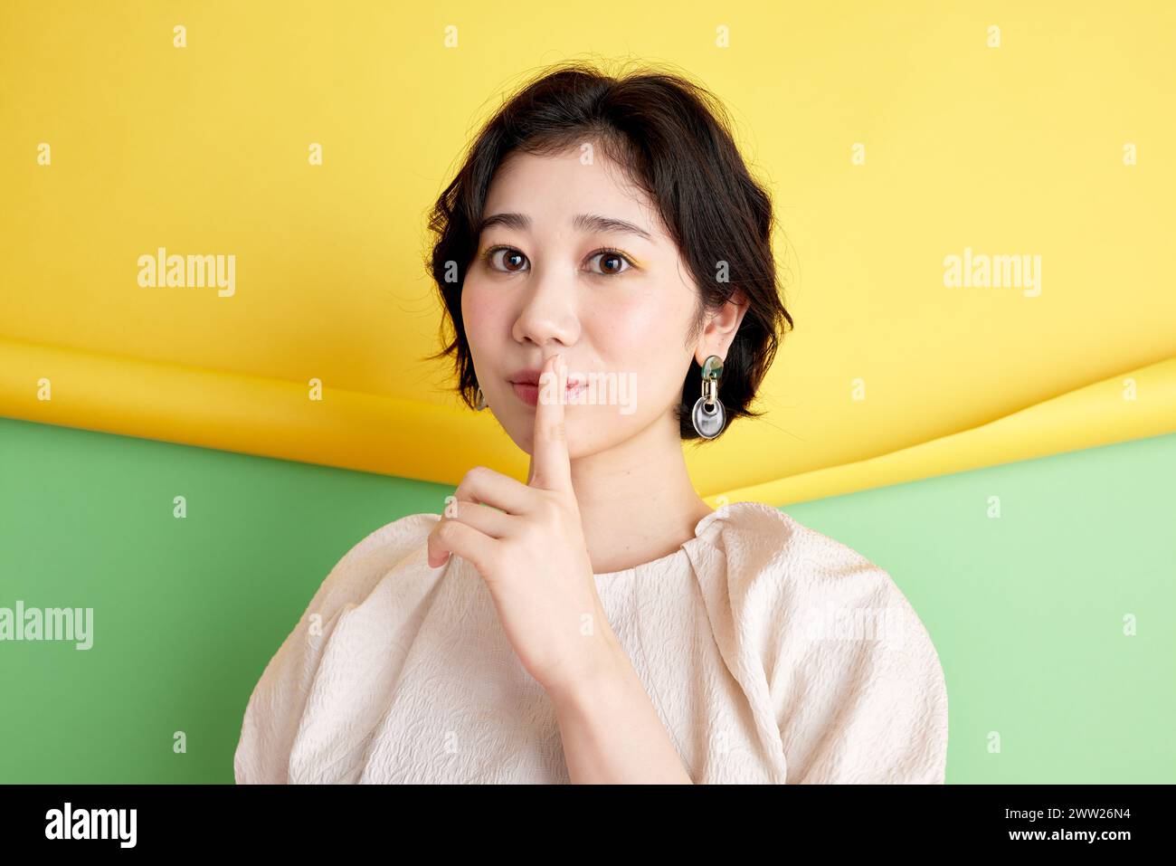 Femme asiatique avec le doigt sur les lèvres sur fond jaune et vert Banque D'Images