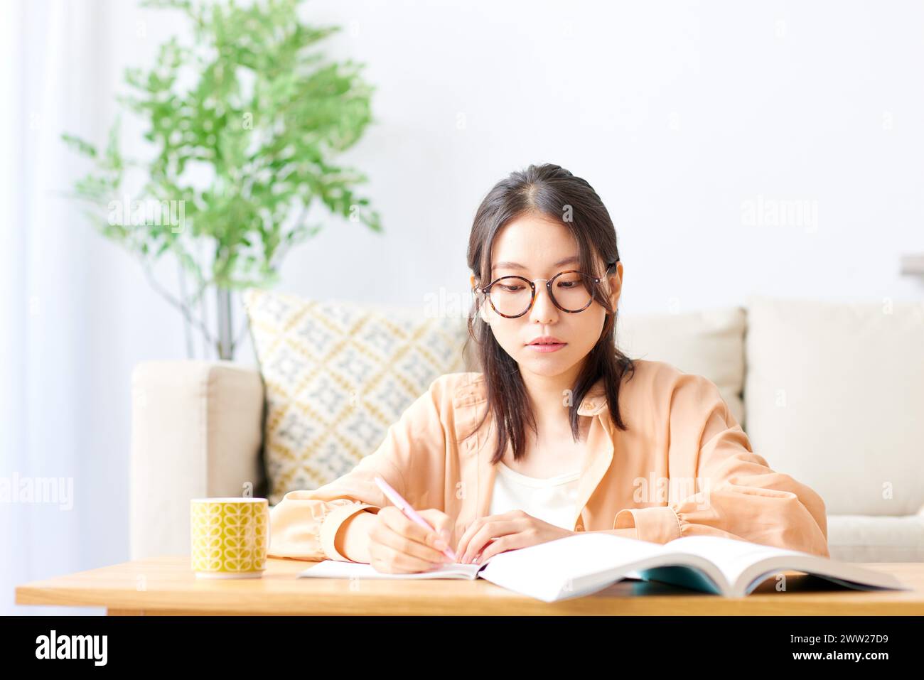 Une femme en lunettes assise à une table avec un livre et un stylo Banque D'Images