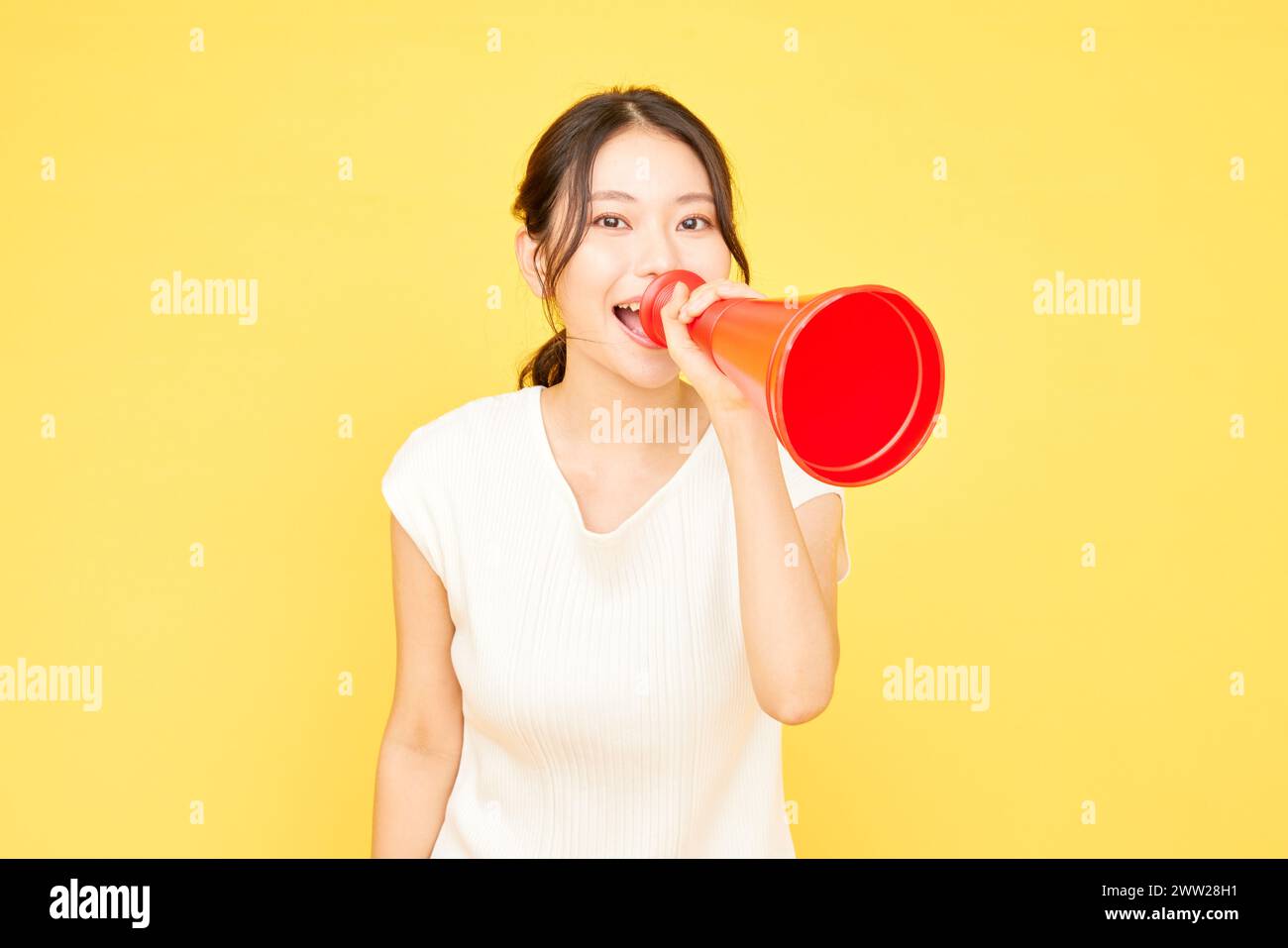 Femme asiatique tenant un mégaphone rouge sur fond jaune Banque D'Images
