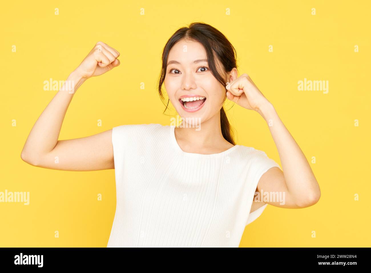 Femme asiatique avec les poings levés sur fond jaune Banque D'Images