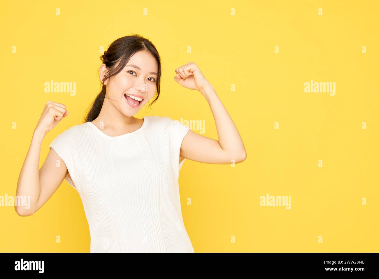 Femme asiatique avec les poings levés sur fond jaune Banque D'Images
