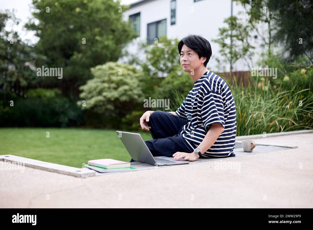 Un homme assis sur un rebord en béton avec un ordinateur portable Banque D'Images