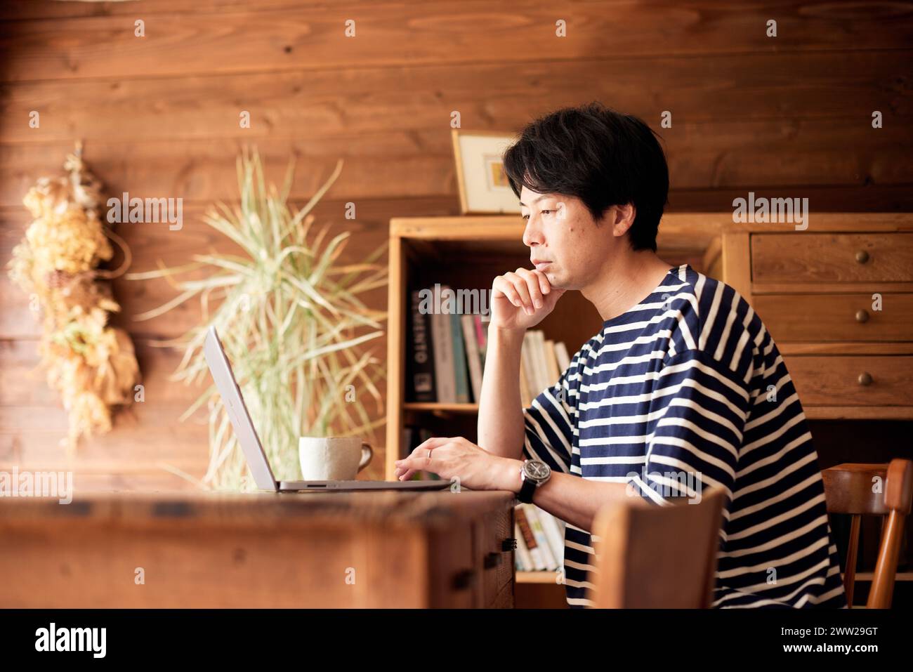 Un homme en chemise rayée assis à un bureau utilisant un ordinateur portable Banque D'Images