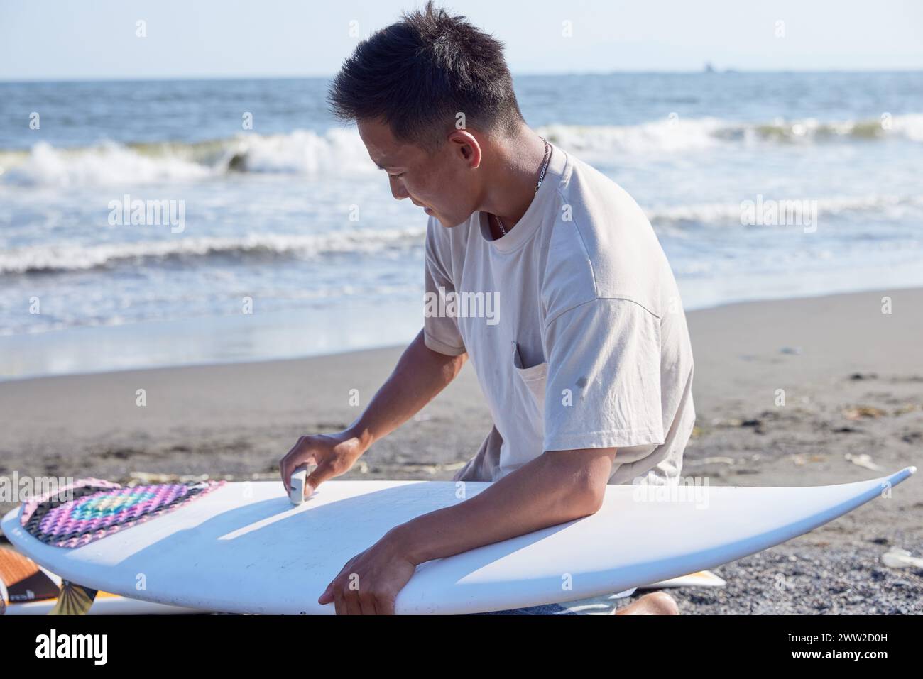 Un homme assis sur la plage avec une planche de surf Banque D'Images