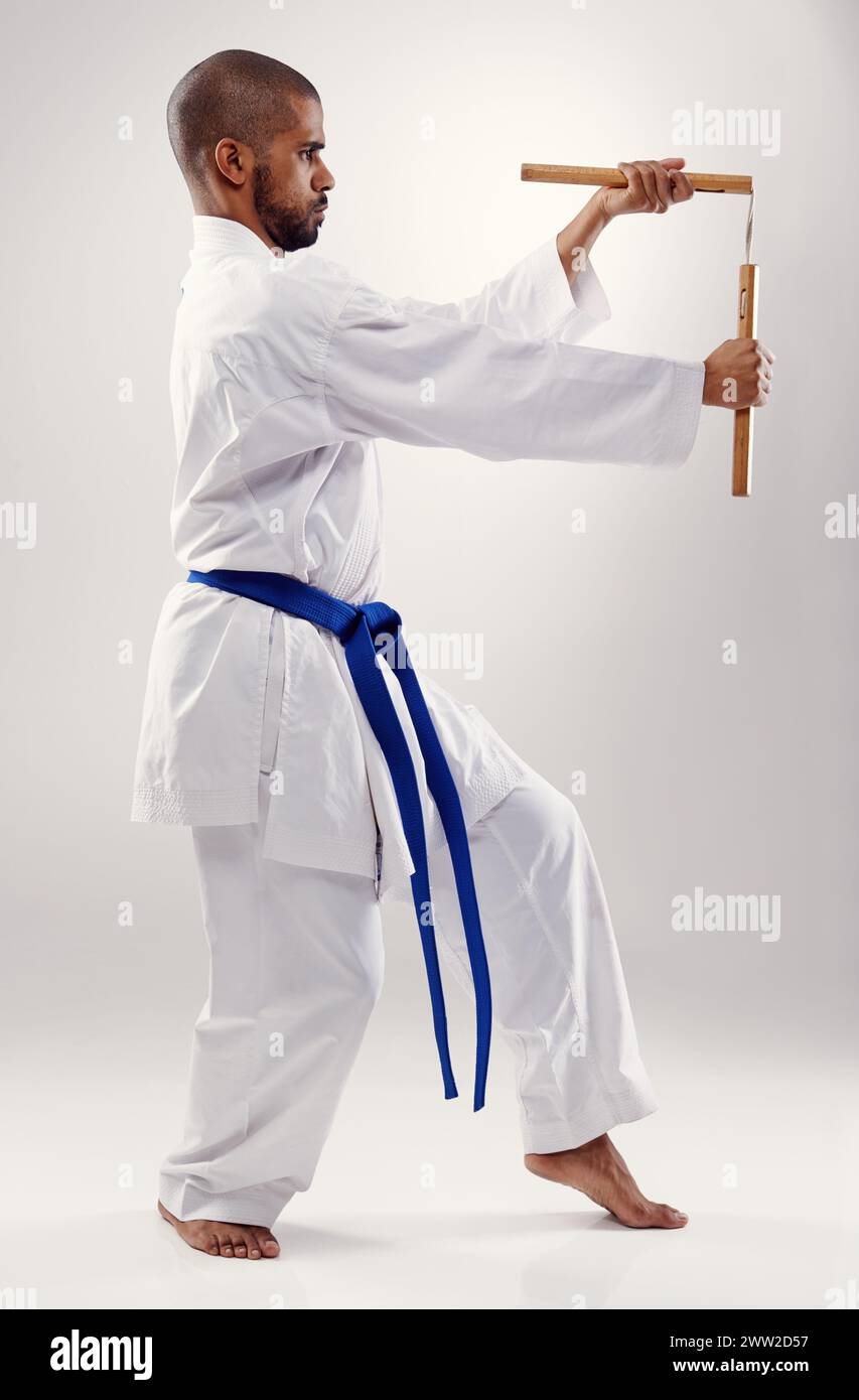 Karaté, combat et homme avec nunchaku dans les arts martiaux, studio ou entraînement avec arme pour la défense sur fond blanc. Nunchucks, exercice et combat Banque D'Images