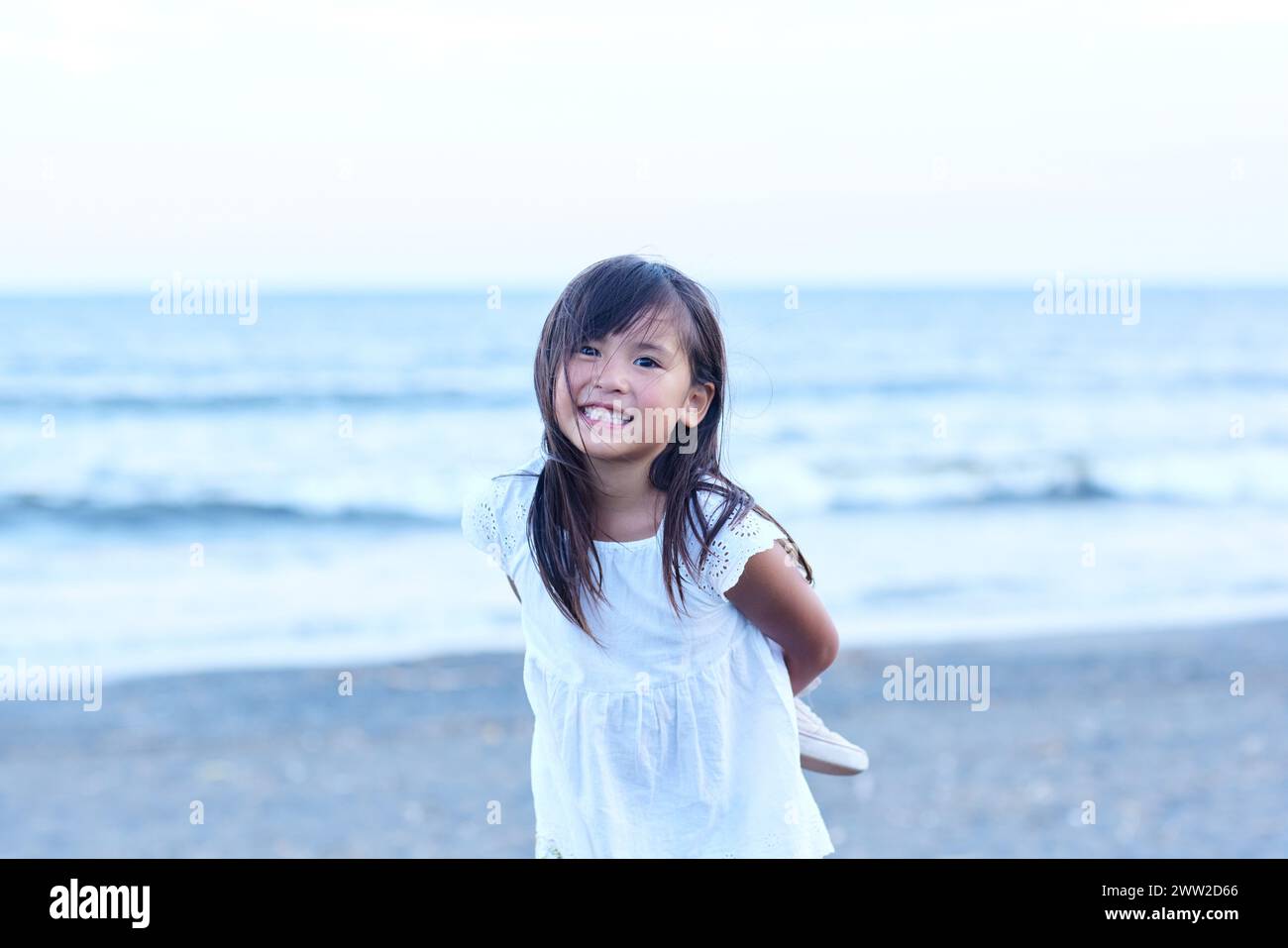 Une petite fille sourit debout sur la plage Banque D'Images