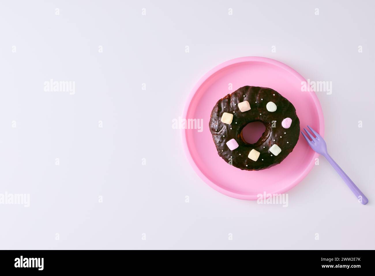 Un beignet au chocolat avec des guimauves sur une assiette rose Banque D'Images