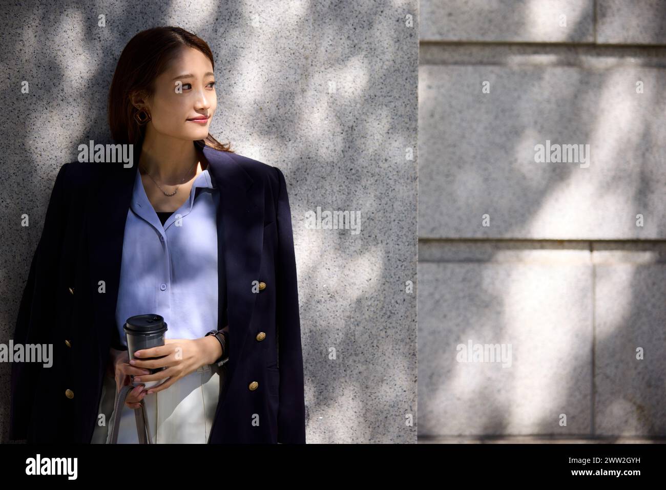 Une femme dans une chemise bleue et une veste appuyée contre un mur Banque D'Images