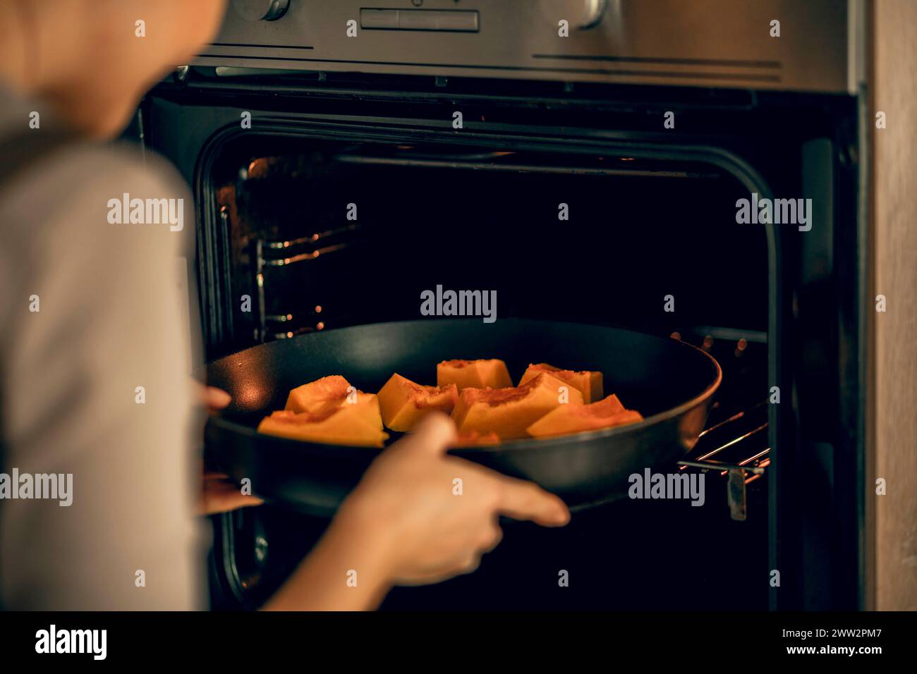 jeune femme dans un tablier met un plat avec de la citrouille dans un four électrique pour la cuisson dans la cuisine Banque D'Images