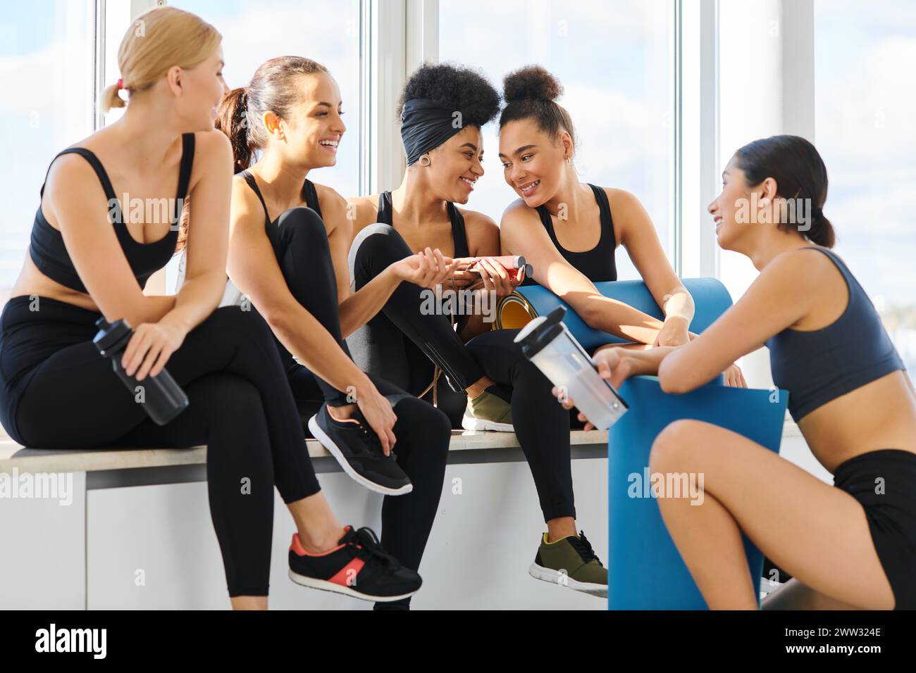 groupe de femmes multiculturelles heureuses et jeunes en vêtements actifs discutant après l'entraînement dans le studio de pilates Banque D'Images