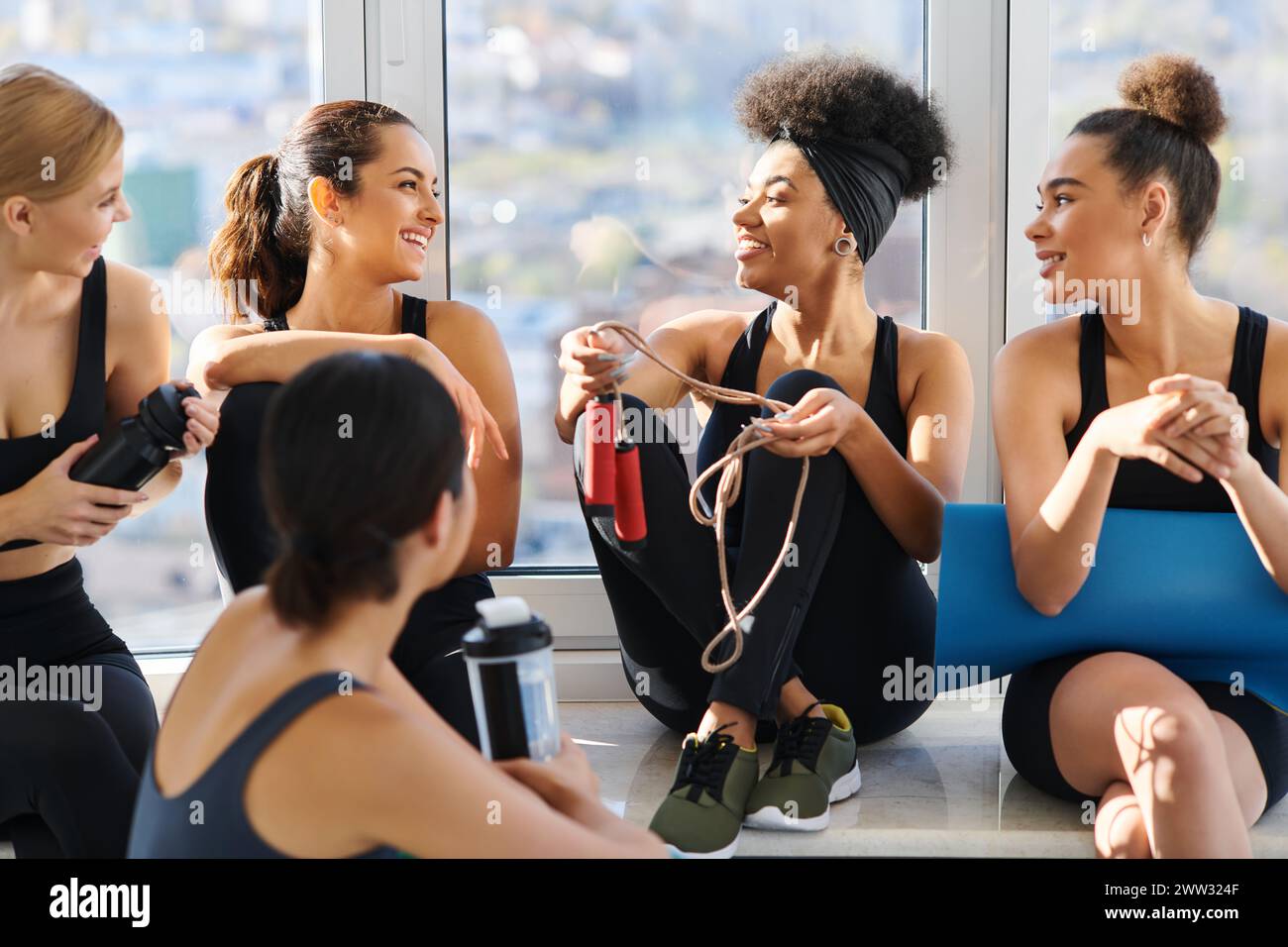 groupe de femmes interraciales heureuses et jeunes en vêtements actifs discutant après l'entraînement dans le studio de pilates Banque D'Images