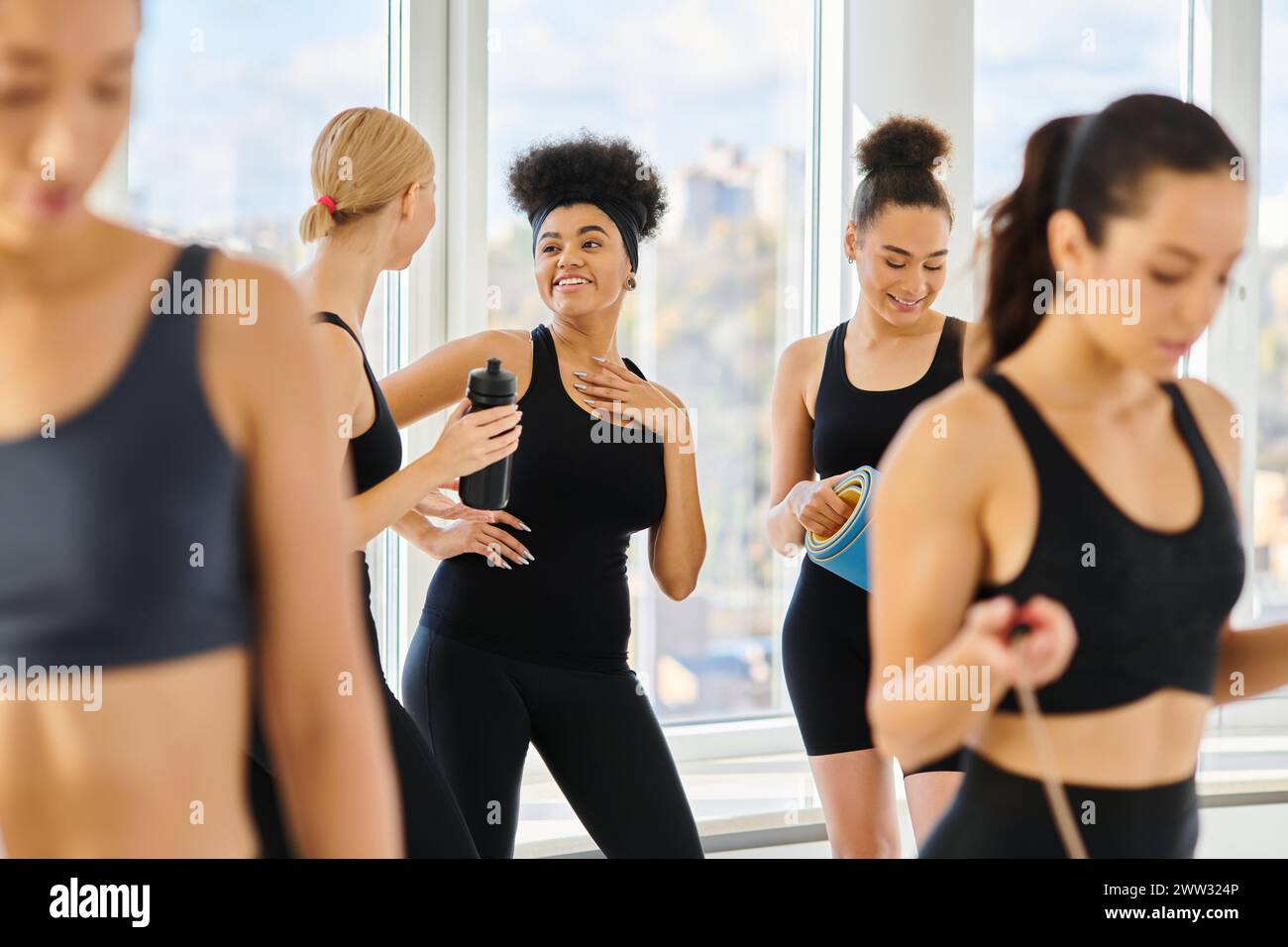 cinq jeunes femmes multiculturelles en vêtements actifs bavardant et souriant après l'entraînement dans le studio de pilates Banque D'Images