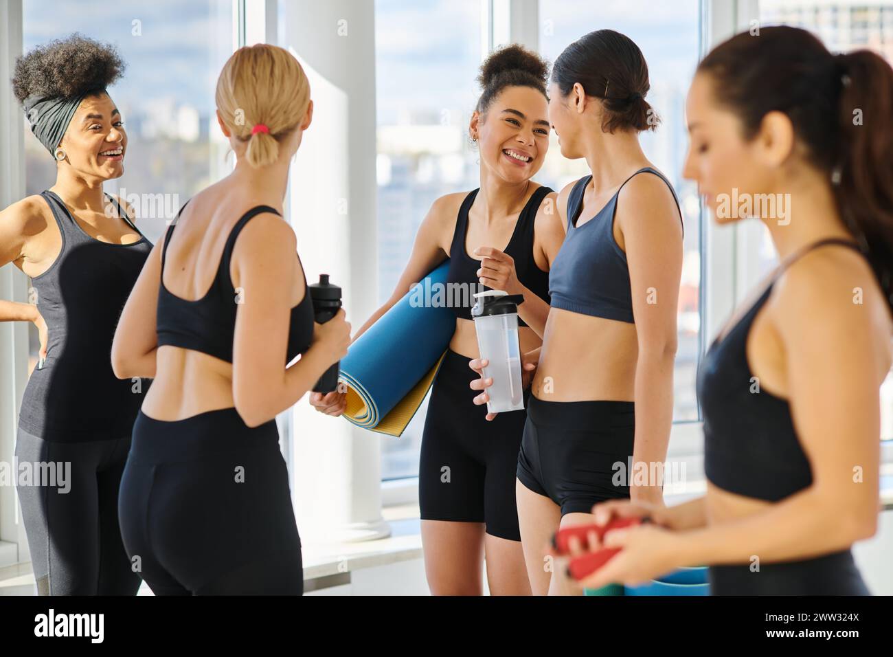 cinq femmes multiculturelles heureuses et jeunes en vêtements actifs discutant après l'entraînement dans le studio de pilates Banque D'Images
