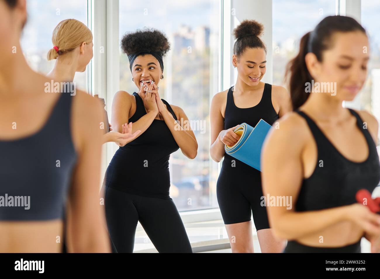 cinq femmes multiculturelles heureuses et jeunes en vêtements actifs discutant après l'entraînement dans le studio de pilates Banque D'Images