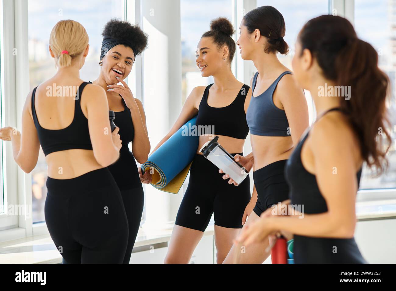 cinq joyeuses et jeunes femmes multiculturelles en vêtements actifs discutant après l'entraînement dans le studio de pilates Banque D'Images