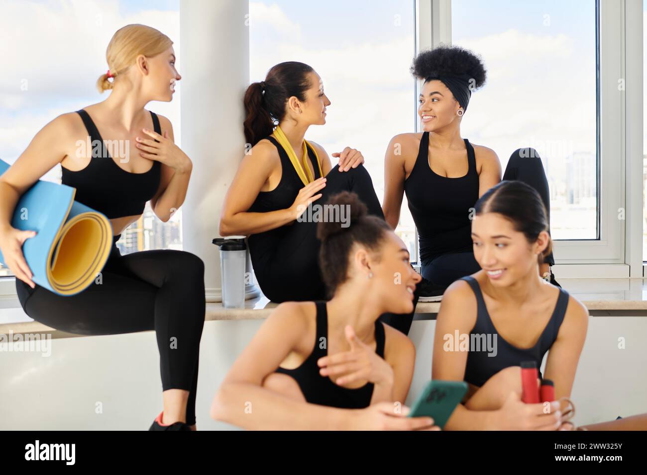 groupe de cinq amies féminines positives en vêtements actifs discutant après l'entraînement dans le studio pilates Banque D'Images