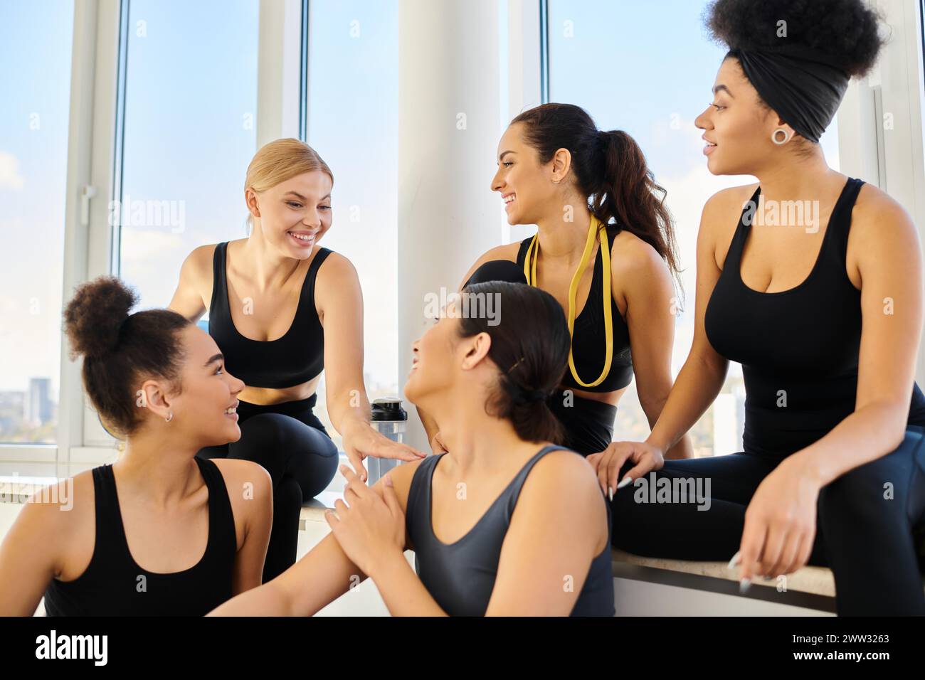 groupe de cinq femmes multiculturelles positives dans les vêtements de sport bavardant après l'entraînement dans le studio de pilates Banque D'Images