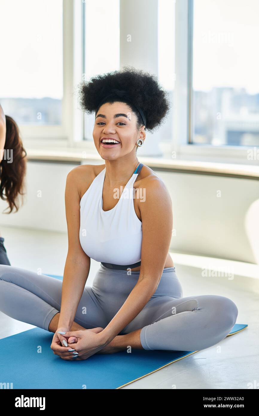 Joyeuse femme afro-américaine dans les vêtements de sport assis sur le tapis et profiter de cours de yoga à l'intérieur Banque D'Images