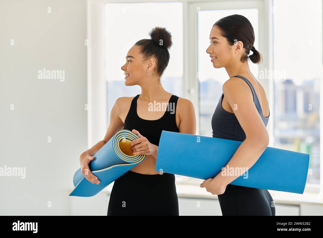 Des femmes heureuses et jeunes dans la vingtaine debout avec des tapis de yoga et souriantes en studio, post-entraînement Banque D'Images