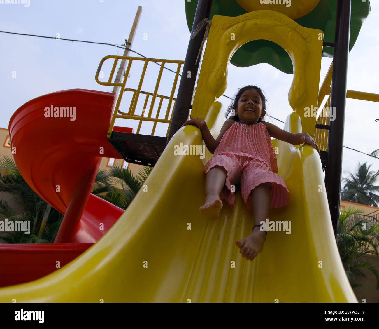Une jeune fille rit avec plaisir alors qu'elle zoome sur un toboggan coloré à une aire de jeux ensoleillée Banque D'Images