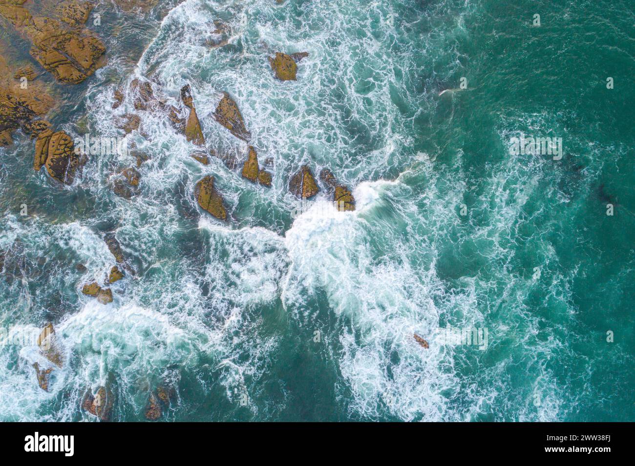 Vue aérienne de haut en bas sur les vagues qui s'écrasent et éclaboussent sur les rochers. Vagues s'écrasant sur la côte rocheuse Banque D'Images