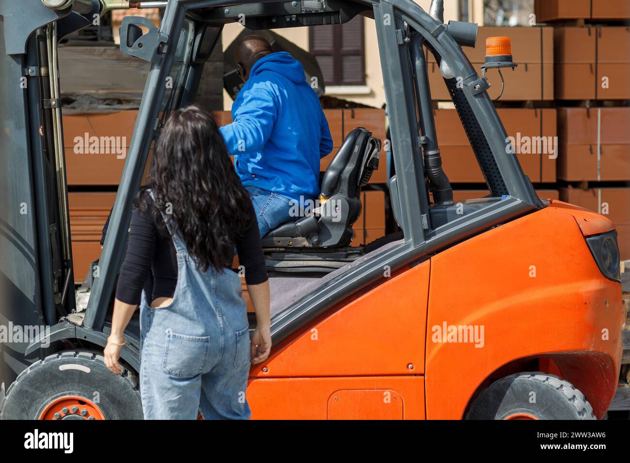Un homme conduisant un chariot élévateur tandis qu'une femme en vêtements de travail observe Banque D'Images