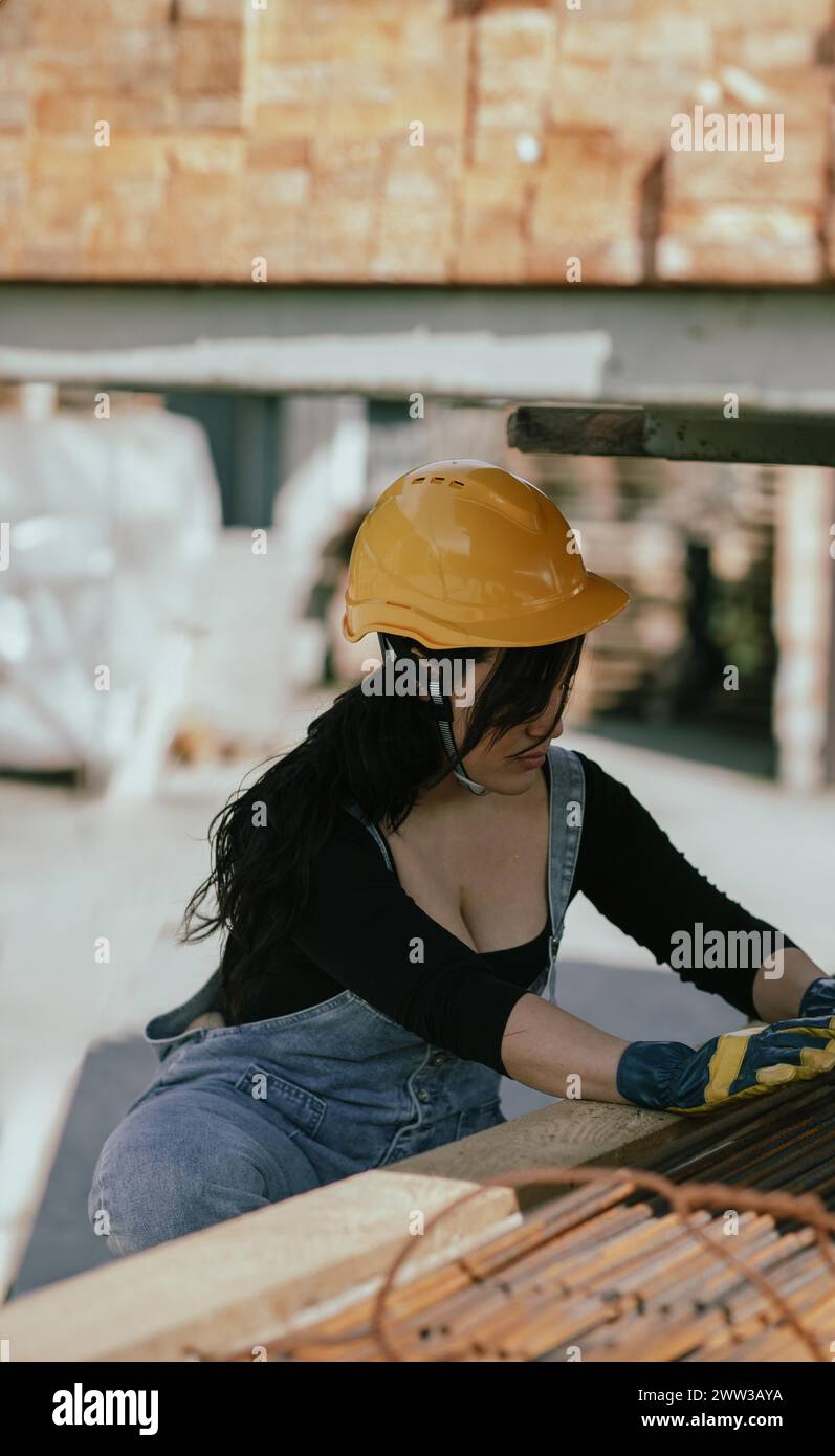 Femme latino concentrée dans l'équipement de sécurité travaillant avec des matériaux de construction Banque D'Images