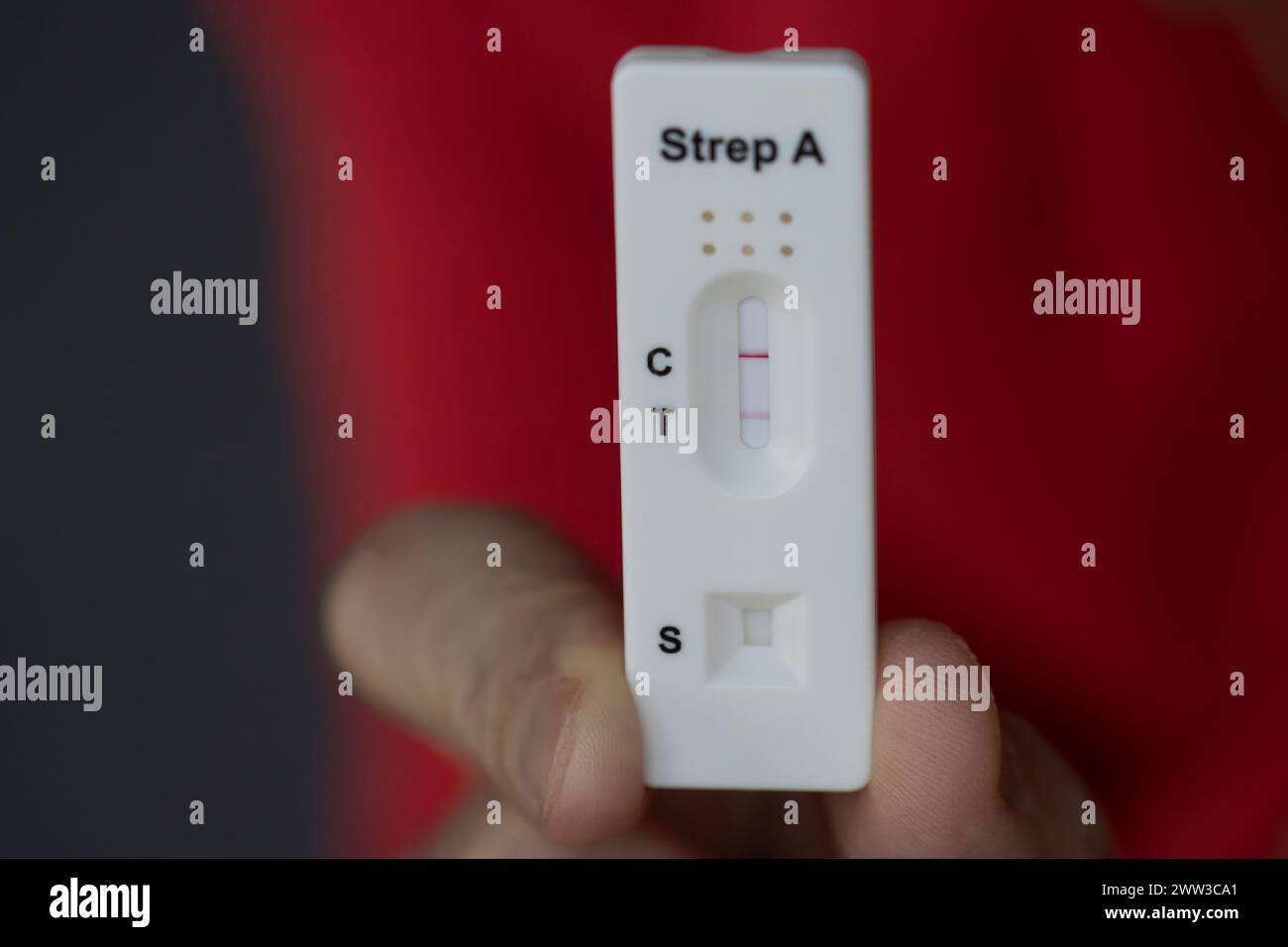 Un gros plan de la main tenant un test de streptocoque positif pendant l'infection, test diagnostique fait à la maison pour la consultation téléphonique avec le médecin. Banque D'Images