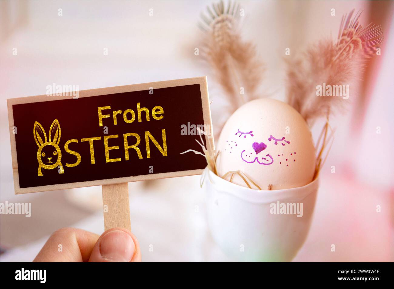 21 mars 2024 : joyeuses salutations de Pâques sur une pancarte devant un œuf de Pâques peint. PHOTOMONTAGE *** Frohe Ostern Gruß zu Ostern auf einem Schild vor einem bemalten Osterei. FOTOMONTAGE Banque D'Images